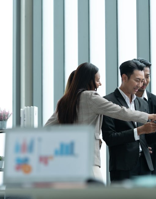 A group of young Asian entrepreneurs A meeting is being held to review stock investment information in a meeting room with natural daylight windows.